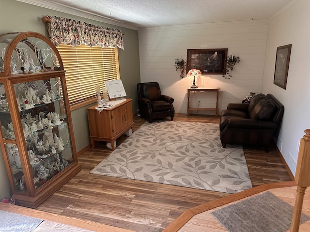 sitting room featuring ornamental molding, wood finished floors, baseboards, a textured ceiling, and wooden walls