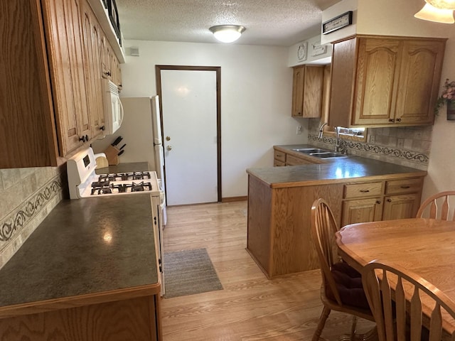 kitchen featuring a sink, white appliances, light wood finished floors, a textured ceiling, and tasteful backsplash