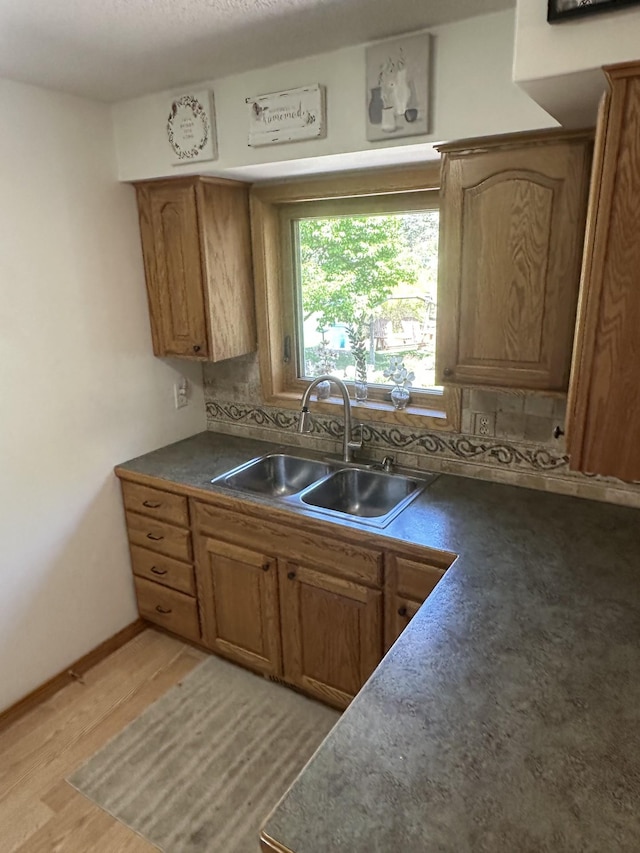 kitchen featuring a sink, backsplash, dark countertops, and brown cabinets