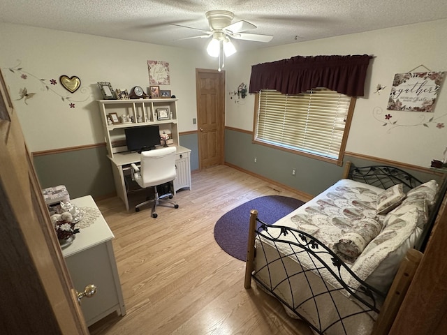 bedroom featuring light wood-style floors, an office area, a textured ceiling, and a ceiling fan