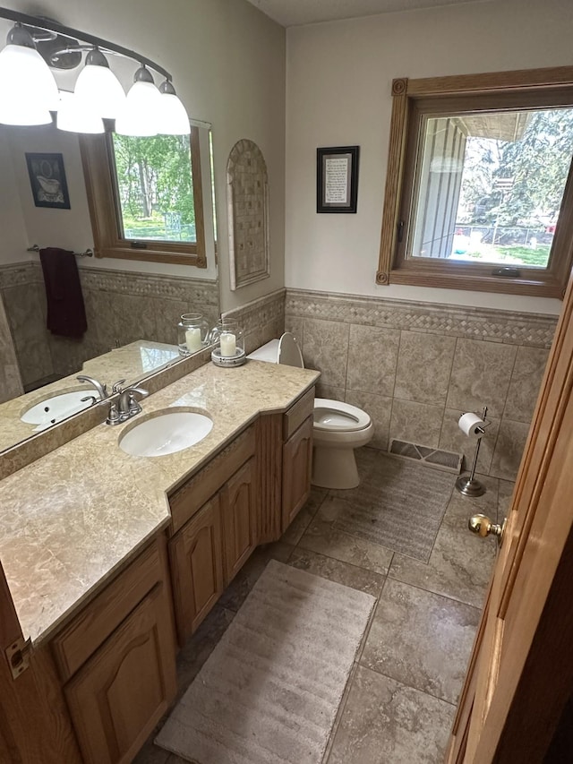 bathroom featuring tile walls, healthy amount of natural light, wainscoting, toilet, and vanity