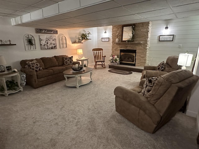carpeted living area with a paneled ceiling, a stone fireplace, and wooden walls
