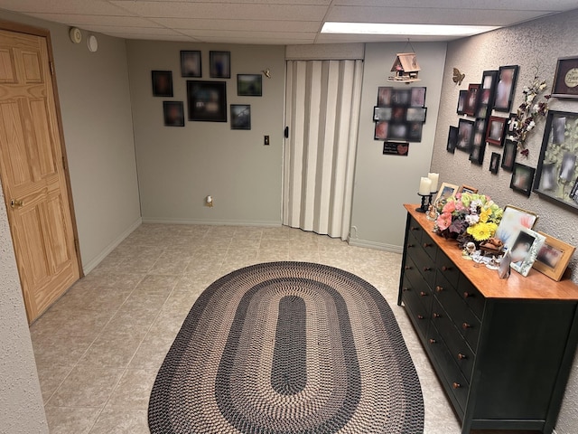 hall featuring a drop ceiling, baseboards, and light tile patterned floors