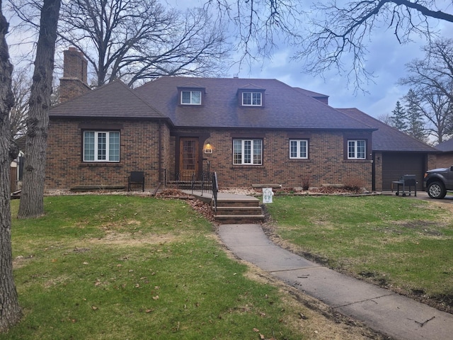 view of front facade with brick siding, a chimney, a garage, and a front lawn
