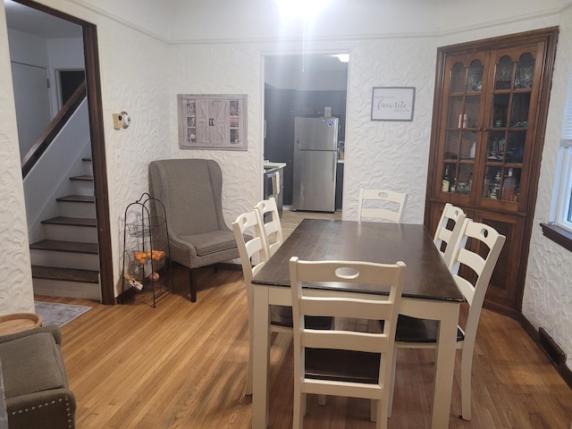 dining room featuring a textured wall, wood finished floors, stairs, and baseboards