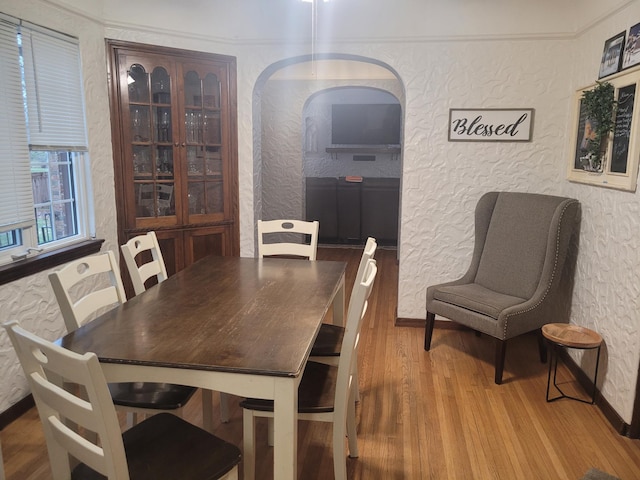 dining area featuring a textured wall, wood finished floors, arched walkways, and baseboards