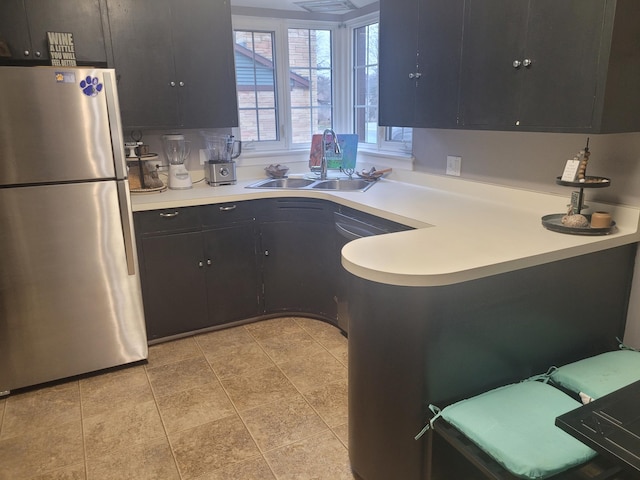 kitchen featuring freestanding refrigerator, a sink, light countertops, dark cabinetry, and a peninsula