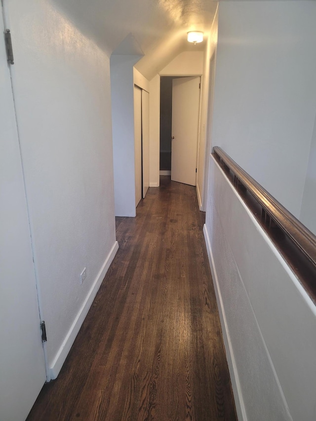 hallway with wood finished floors, lofted ceiling, and baseboards