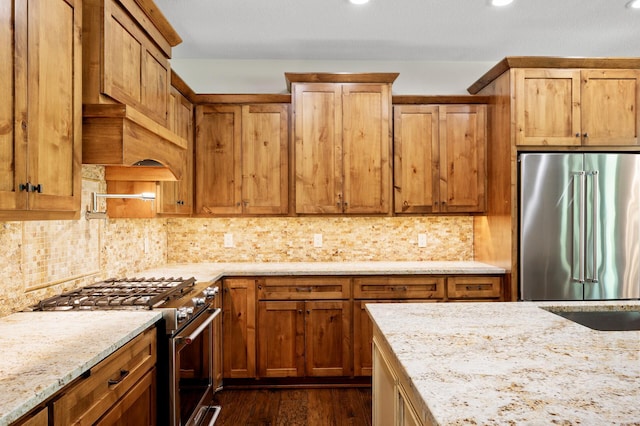 kitchen featuring high end appliances, backsplash, light stone countertops, dark wood-type flooring, and recessed lighting