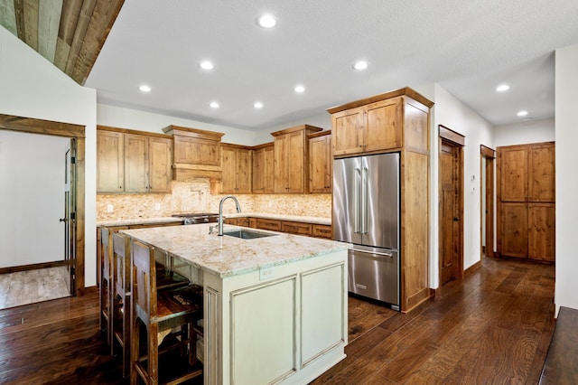 kitchen featuring high end refrigerator, dark wood-style flooring, a sink, light stone countertops, and recessed lighting