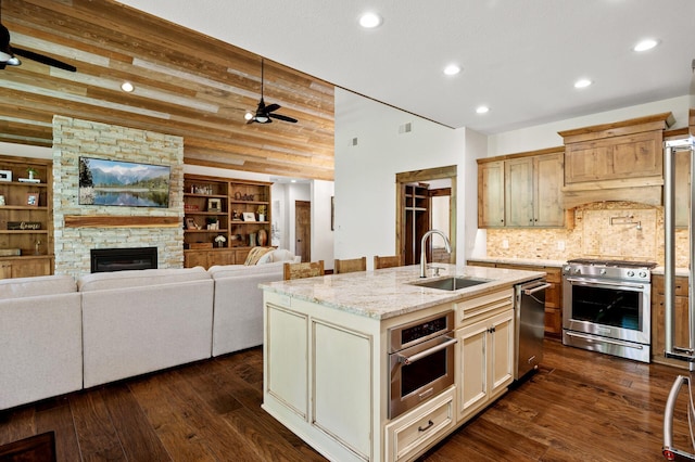 kitchen with stainless steel appliances, a sink, a ceiling fan, dark wood-style flooring, and light stone countertops
