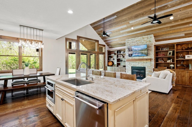 kitchen featuring a sink, stainless steel appliances, ceiling fan, vaulted ceiling, and a stone fireplace