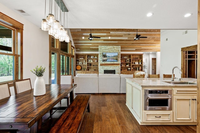 kitchen featuring ceiling fan, a sink, stainless steel oven, dark wood finished floors, and light stone counters