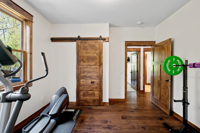 workout area with dark wood-style floors, a barn door, baseboards, and a textured ceiling