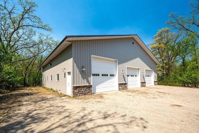 view of side of home featuring stone siding, a detached garage, and an outbuilding