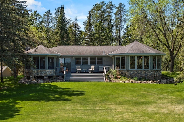 rear view of house featuring a sunroom, stone siding, a lawn, and roof with shingles