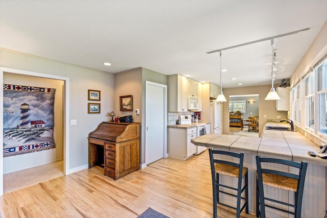 kitchen with track lighting, a sink, light wood-style flooring, a breakfast bar area, and white appliances