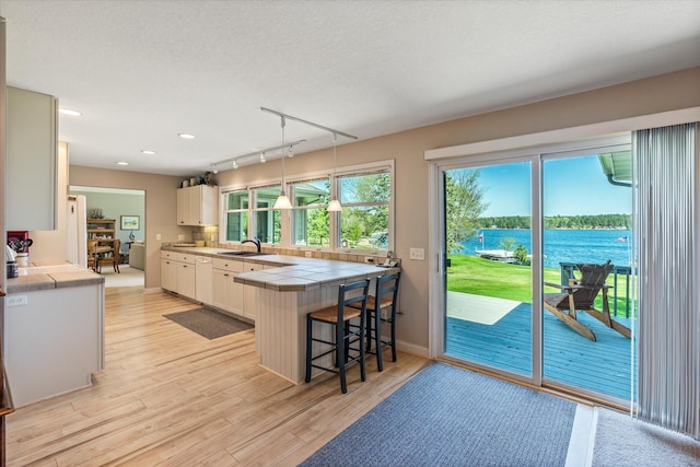 kitchen featuring tile counters, white cabinets, light wood finished floors, a breakfast bar area, and a water view