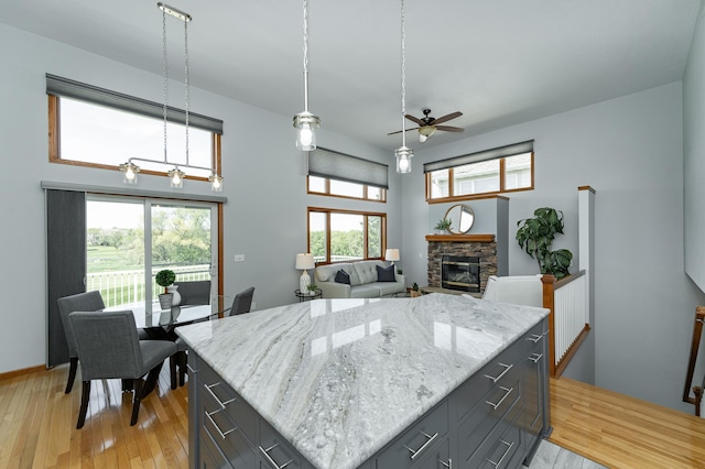 kitchen featuring a fireplace, ceiling fan, light wood-type flooring, light stone counters, and gray cabinets