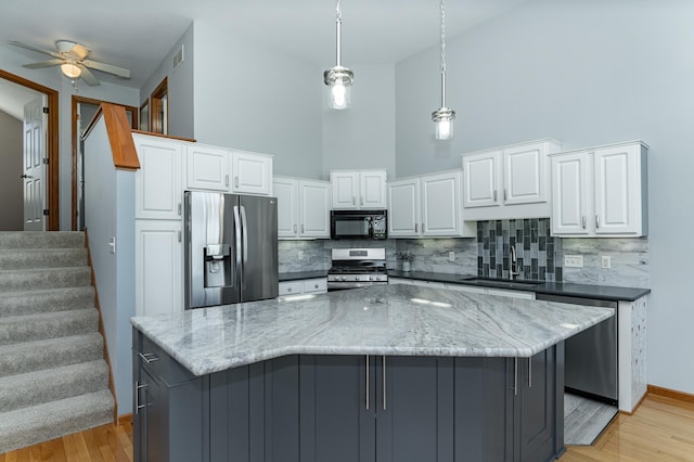 kitchen featuring appliances with stainless steel finishes, a sink, decorative backsplash, a towering ceiling, and white cabinets