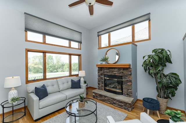 living room featuring ceiling fan, a stone fireplace, wood finished floors, and baseboards