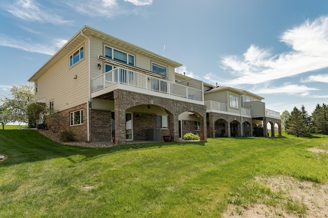 rear view of house featuring brick siding, a yard, a balcony, and central AC unit