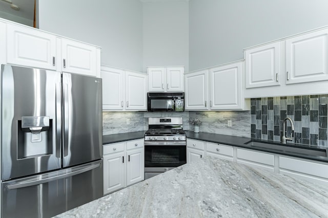 kitchen featuring stainless steel appliances, a sink, backsplash, white cabinets, and dark stone countertops
