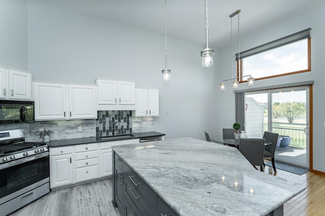 kitchen with black microwave, stainless steel range with gas cooktop, a sink, a high ceiling, and decorative backsplash