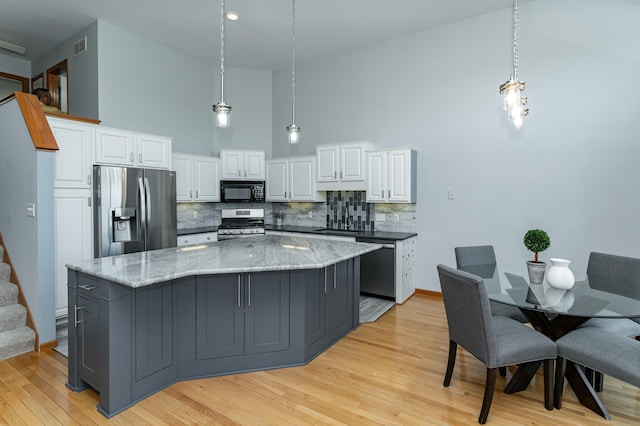 kitchen with stainless steel appliances, a sink, tasteful backsplash, white cabinetry, and light wood-style flooring