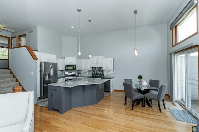 kitchen featuring appliances with stainless steel finishes, a towering ceiling, white cabinetry, a center island, and light wood finished floors
