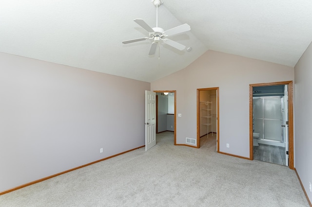 unfurnished bedroom featuring lofted ceiling, a spacious closet, light carpet, baseboards, and connected bathroom