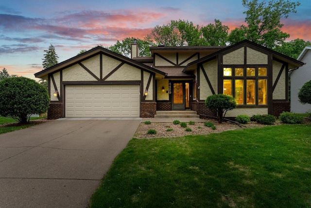 tudor-style house featuring a garage, concrete driveway, brick siding, a front yard, and stucco siding