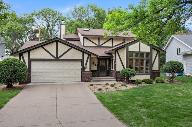 english style home with stucco siding, an attached garage, brick siding, and a front yard