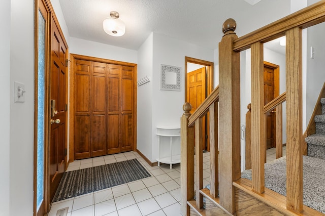 foyer entrance with stairs, light tile patterned floors, a textured ceiling, and baseboards