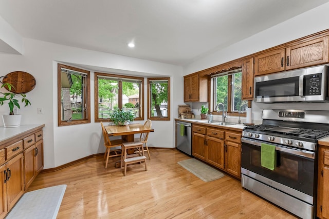 kitchen with stainless steel appliances, a sink, brown cabinetry, light countertops, and recessed lighting