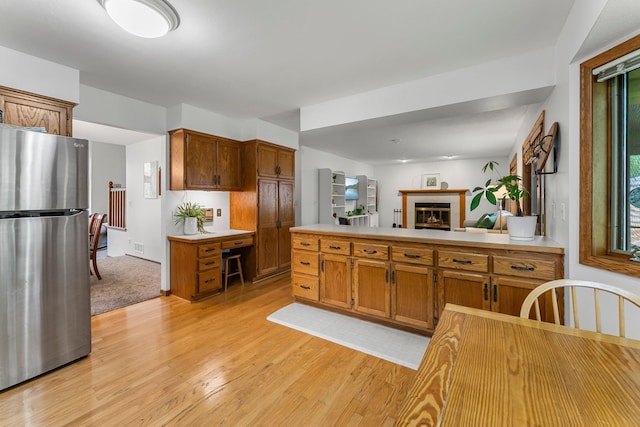 kitchen featuring freestanding refrigerator, light wood finished floors, light countertops, and brown cabinetry