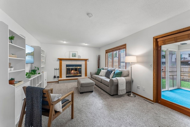 living room featuring baseboards, carpet flooring, a tile fireplace, and a textured ceiling