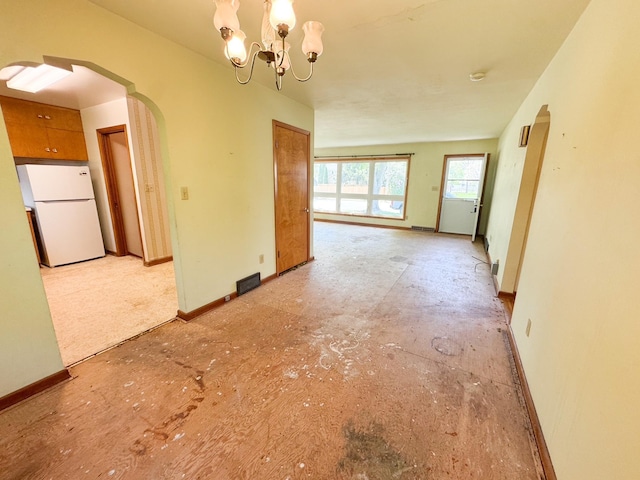 spare room featuring arched walkways, a chandelier, and baseboards