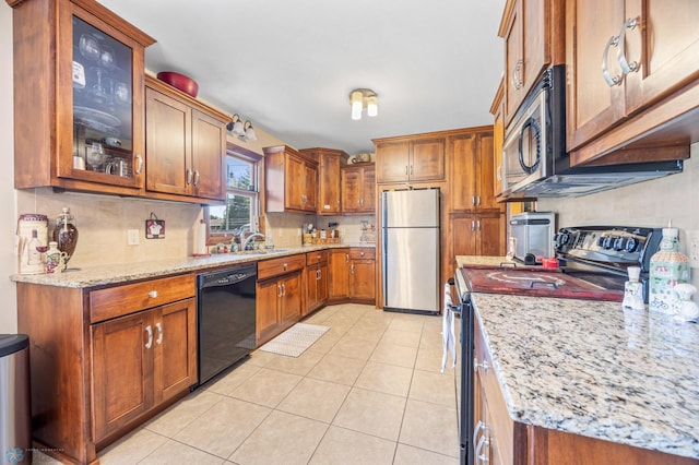 1214 8th St N, Moorhead, MN 56560 - kitchen with stainless steel appliances, brown cabinets, light stone counters, light tile patterned flooring, and glass insert cabinets