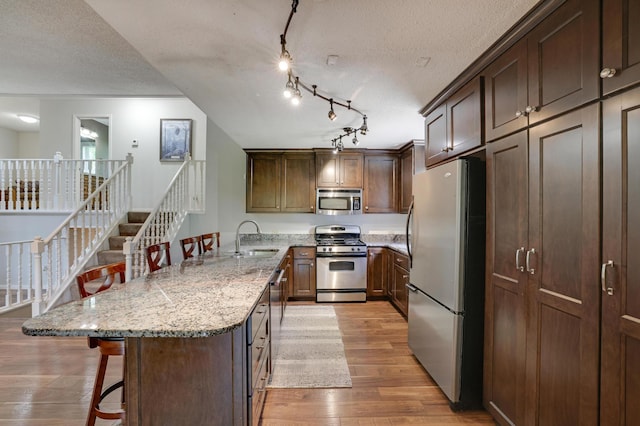 7256 Maciver Ave NE, Otsego, MN 55301 - kitchen with appliances with stainless steel finishes, a sink, light wood-style floors, a breakfast bar area, and a peninsula