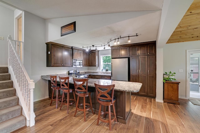 7256 Maciver Ave NE, Otsego, MN 55301 - kitchen with appliances with stainless steel finishes, a peninsula, dark brown cabinets, light wood-type flooring, and light stone countertops