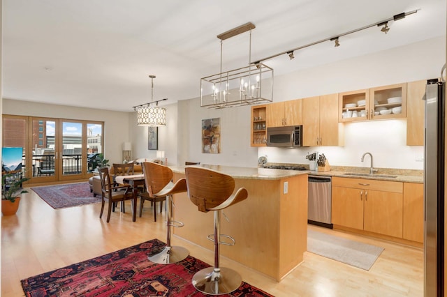 kitchen featuring a sink, appliances with stainless steel finishes, light wood-type flooring, glass insert cabinets, and a kitchen breakfast bar