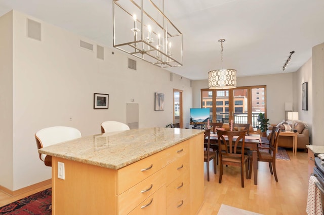 kitchen featuring light brown cabinetry, light wood-type flooring, open floor plan, decorative light fixtures, and light stone counters