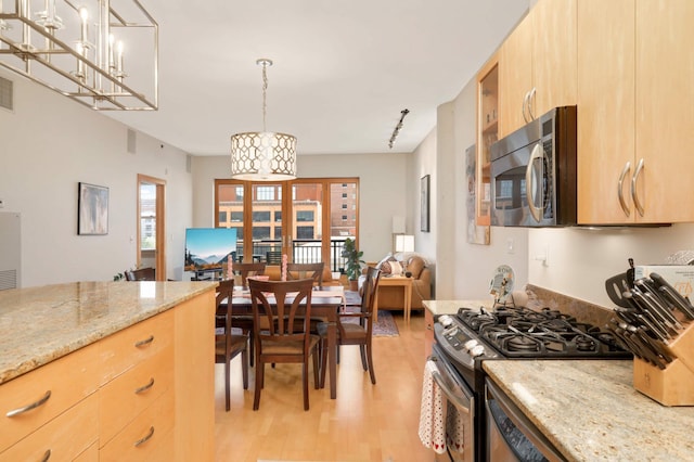 kitchen featuring appliances with stainless steel finishes, light brown cabinets, light wood finished floors, light stone countertops, and hanging light fixtures