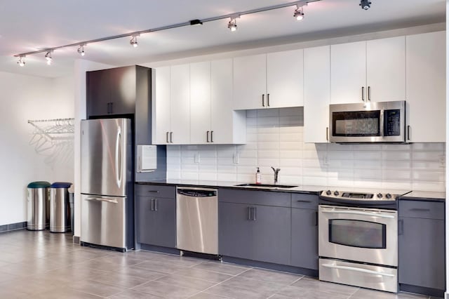 kitchen with appliances with stainless steel finishes, a sink, dark countertops, and track lighting