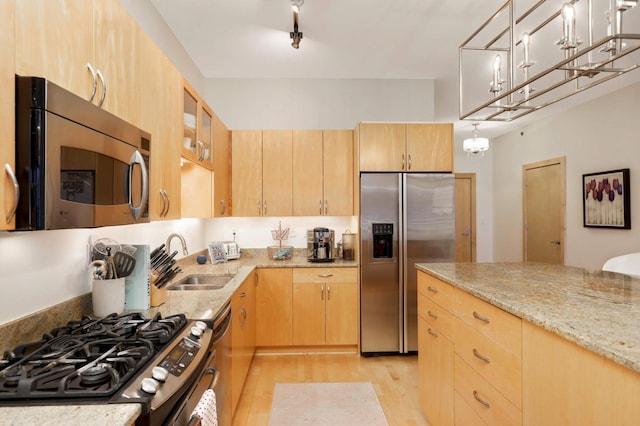 kitchen featuring appliances with stainless steel finishes, light brown cabinets, a sink, light wood-style floors, and light stone countertops