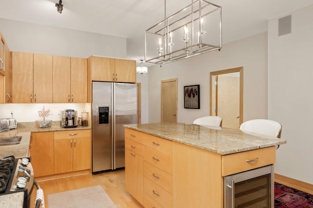 kitchen featuring stainless steel appliances, beverage cooler, light brown cabinetry, and light wood finished floors
