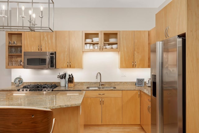 kitchen featuring stainless steel appliances, a sink, light stone counters, glass insert cabinets, and decorative light fixtures