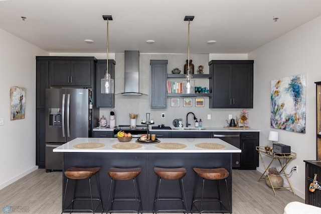 kitchen featuring wall chimney range hood, stainless steel appliances, a sink, light countertops, and a breakfast bar area
