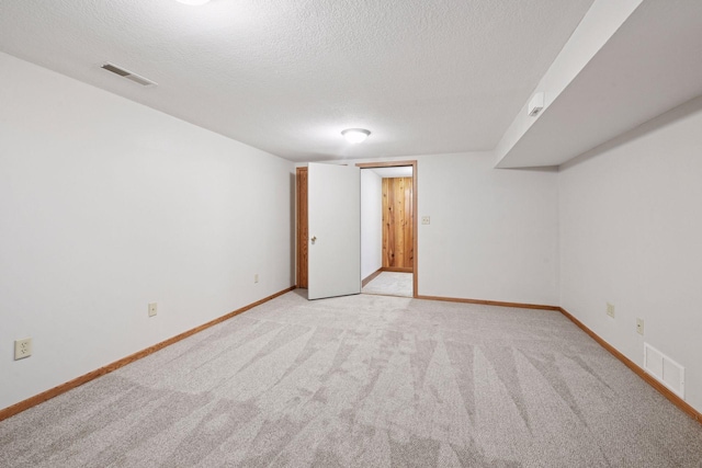 spare room featuring a textured ceiling, light colored carpet, and baseboards